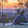 A portrait of a couple drinking wine at sunset on a picnic at Mount Gravatt Lookout in Brisbane.