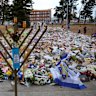A menorah frames flowers laid in grief a week after the December 14 massacre at Bondi Beach. Calls have grown for a deeper investigation of the attack.