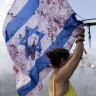 A woman holds an Israeli flag with red paint on it to resemble blood as protesters block a main road during a rally calling for a hostages deal on September 13, 2024 in Tel Aviv, Israel.