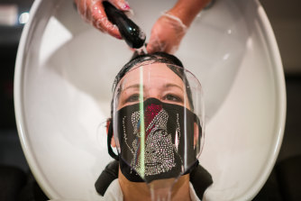 A woman wears a protective mask as she has her hair washed in London. Research indicates a headache is the most common symptom of the virus.