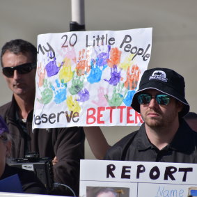 A teacher with a sign including the handprints of students in their class. 