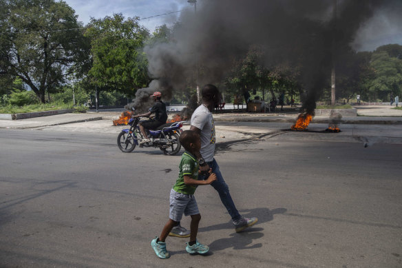 A man and a child walk by burning tires on a street on Sunday in Port-au-Prince, Haiti, where a group of 17 missionaries, including children, was kidnapped by a gang.