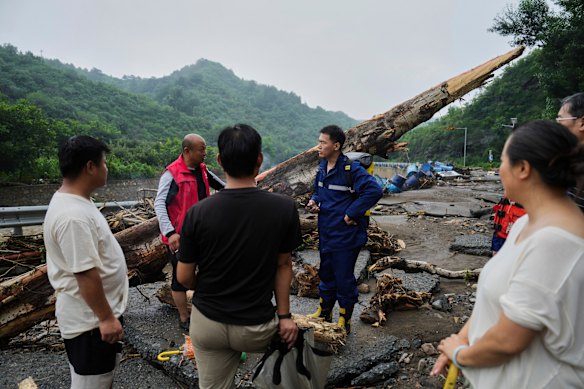 In this photo released by Xinhua News Agency, rescuers talk to villagers on a road damaged by floodwaters in Miyun District 
