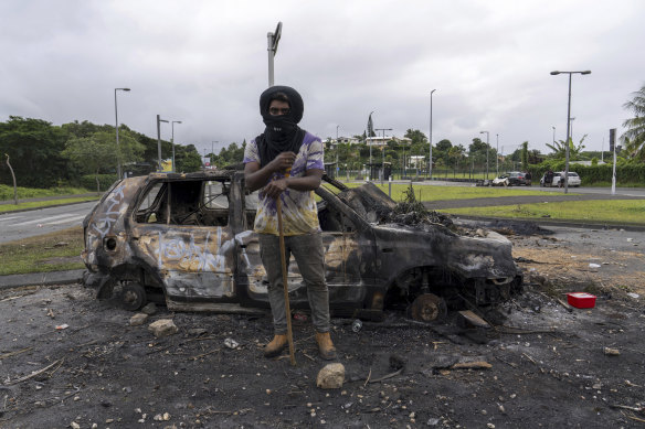 A man stands in front of a burnt car after unrest in Noumea, New Caledonia this week.