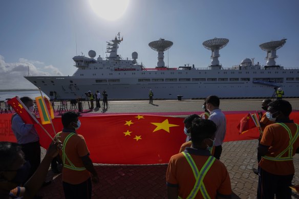 Sri Lankan port workers hold a Chinese national flag to welcome Chinese research ship Yuan Wang 5 as it arrives in Hambantota, Sri Lanka.