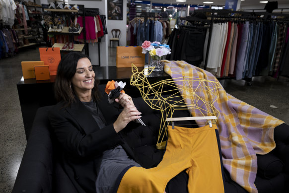 Tanya Vella with some paper flowers, empty bags and boxes from Hermes and Louis Vuitton, Kill Bill style pants, a metal animal sculpture and old blankets that are being purchased to be upcycled into clothes, at Vinnies in Surry Hills, Sydney.