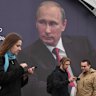 People at a book festival in St Petersburg walk in front of a poster of Russian President Vladimir Putin on Thursday.