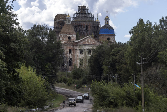 Ukrainian military vehicles pass a villager on a bicycle and a church in the village of Yunakivka in the Sumy region of Ukraine.