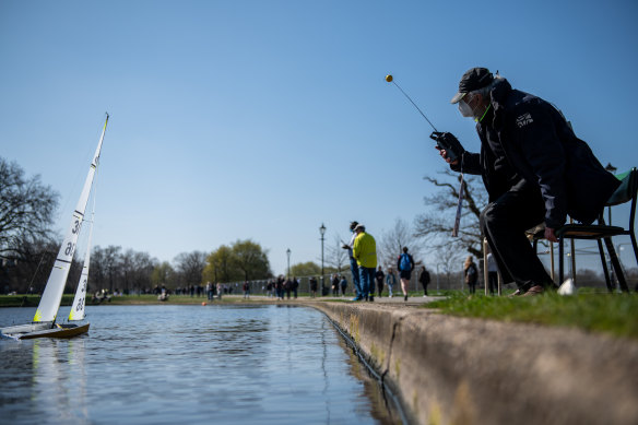 A man wearing a face mask operates a remote control boat on a pond in Clapham Common in London. The British government has eased rules on socialising, permitting groups of six people (or more if limited to two households) to meet outdoors.