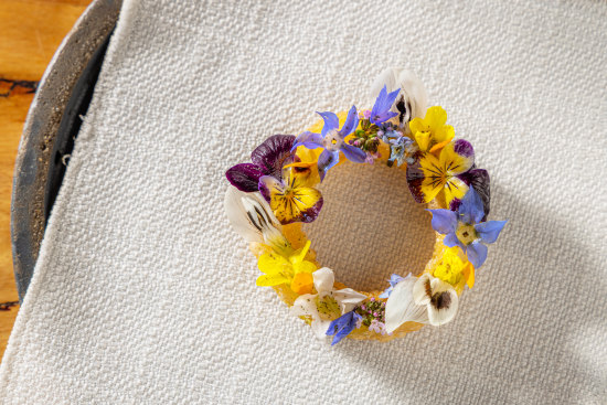 Fried pastry ring drizzled with green garlic oil and topped with edible flowers.