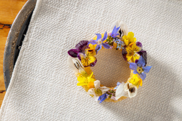 Fried pastry circle filled with horseradish and  buttermilk gel, drizzled with green garlic oil and topped with edible flowers.