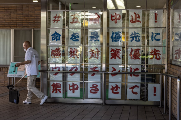 A cleaner works next to a protest banner displayed in the window of a hospital near the Tokyo Olympic Stadium that reads “Stop Tokyo Olympics. Prioritise saving lives. Concentrate on COVID vaccine”.