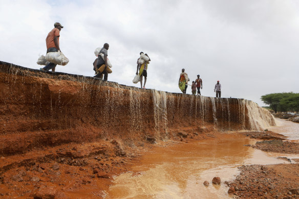 People walk on a destroyed section of the road following heavy rains which stopped vehicles from crossing along Mwingi-Garissa highway, Northern Kenya.