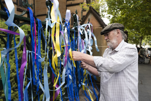 Survivor Paul Auchettl ties a ribbon at St Mary’s Cathedral. 