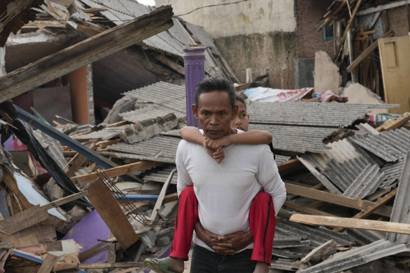 A man carries his son past ruins of houses damaged in Monday’s earthquake in Cianjur.