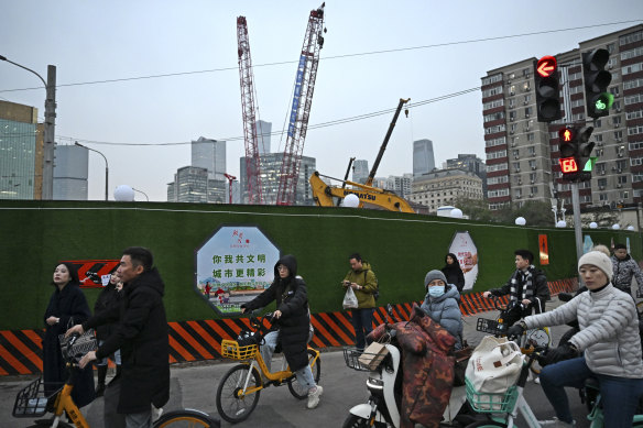 People commuting by bicycle ride past a construction site during rush hour in Beijing.