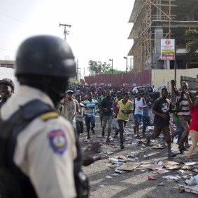 A police officer looks on as a crowd enters the Delimart supermarket complex, which had been burned during two days of protests against a planned hike in fuel prices in Port-au-Prince, 