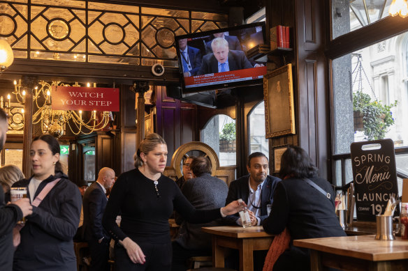 People sit in the Red Lion pub as former prime minister Boris Johnson giving evidence on partygate is shown on the TV.