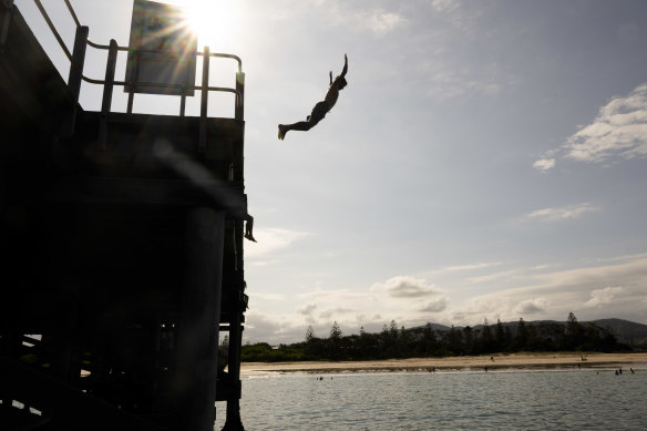 Teenagers jump off the Coffs Harbour jetty, with the foreshore in the background.