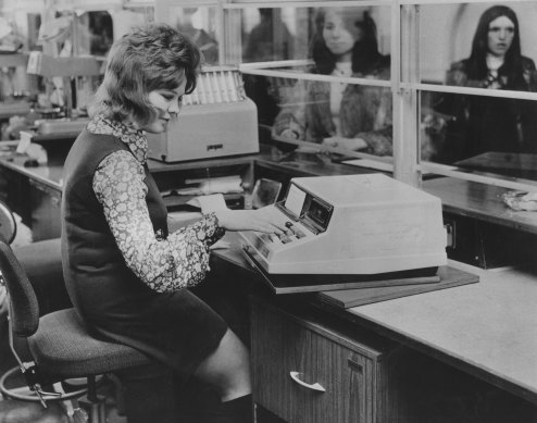 A bank teller uses a Chequemaster machine, designed for cashing cheques and handling savings withdrawals, in 1972.