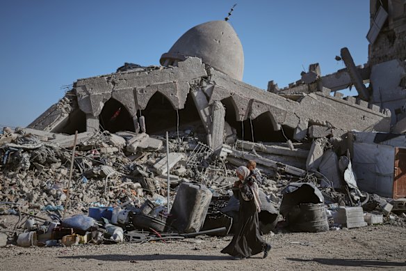 A Palestinian woman carrying her child walks past a destroyed mosque in Gaza City.