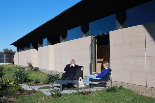 Rob and Sally Hawkins sitting near the massive rammed earth wall on the eastern side of the Mystery Bay home. The house, designed by their son, architect Jack Hawkins, is one of the finalists in this year’s Australian Institute of Architects’ NSW award for best new house. 