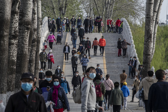 People wear protective masks as they walk while enjoying the spring weather on April 5, 2020  at a park in Beijing.