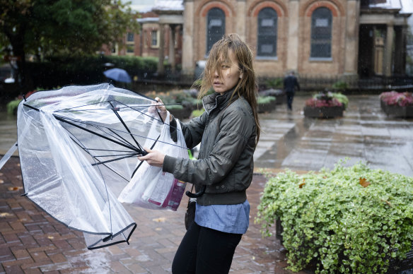 A wet pedestrian struggles with her umbrella in the rain in Sydney