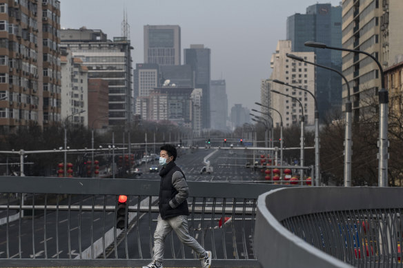 A man wears a protective mask as he crosses a footbridge over a nearly empty road in a residential neighbourhood in Beijing.