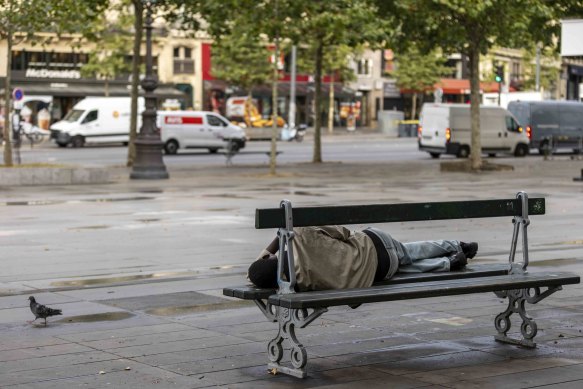 A homeless person sleeps on a bench in downtown Paris.