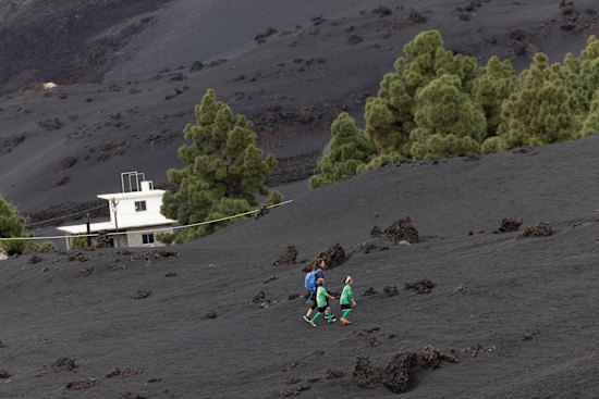 A family walks up a hill to a football field in the Las Manchas area of La Palma through an area entirely carpeted with volcanic ash.