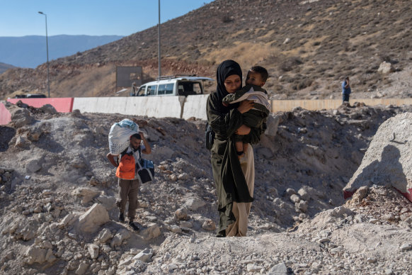 A woman carries a child through the crater from an Israeli air strike as she makes her way across the border with her children.