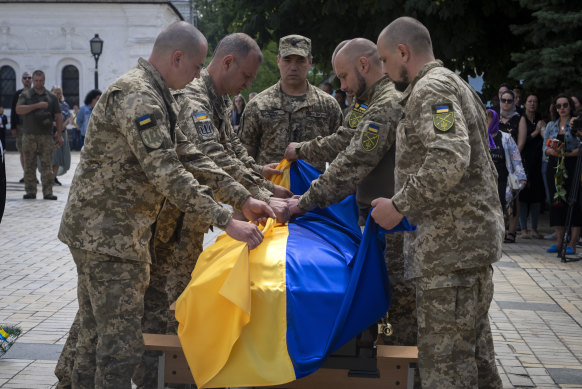 Soldiers fold a Ukrainian flag on the coffin of a colleague killed by the Russian troops in Kyiv, Ukraine.