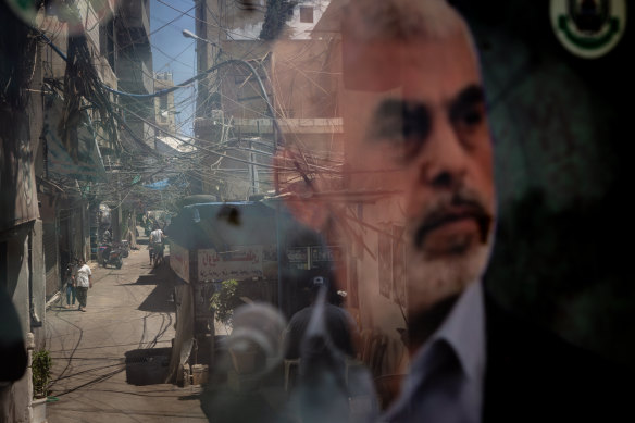 People are reflected in a window displaying a poster of newly appointed Hamas leader Yahya Sinwar in the Palestinian camp of Bourj al-Barajneh in Beirut Lebanon.