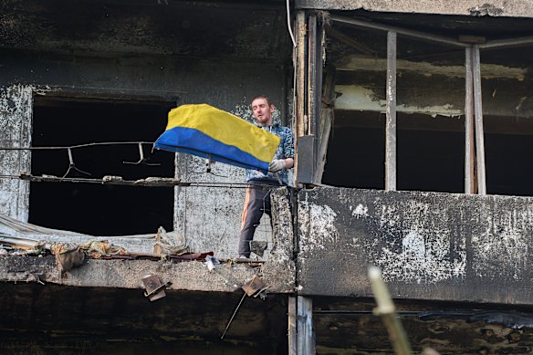 A man hangs out the national flag at his damaged apartment balcony in Kyiv.