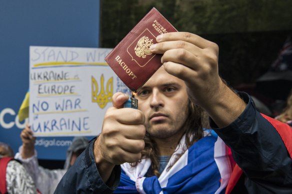 A man draped in the Russian flag attempts to burn a passport during the Stop War in Ukraine rally.
