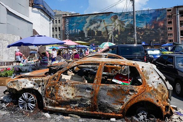 Questo mese la gente compra cibo in un mercato all’aperto improvvisato a Kiev, tra auto ed edifici danneggiati dagli attacchi russi.