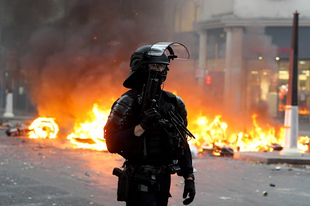 A police officer wearing riot gear stands in front of a burning barricade during a demonstration near Place de la République.