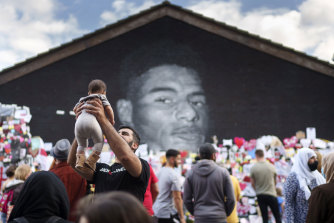 A man holds a child in the air as crowds gather at the Marcus Rashford mural in Manchester.