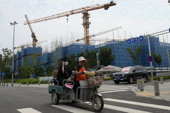 Residents on a tricycle ride past a car with a sign that reads “Country Garden homeowners rights protections car”, parked near homeowners camping outside the Country Garden One World City project on the outskirts of Beijing.