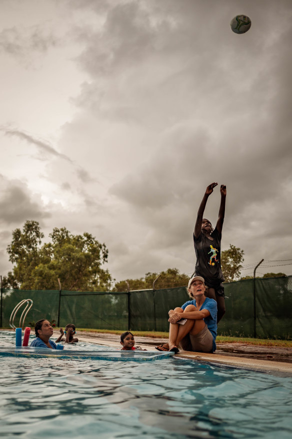 A child throws a ball in the air near the remote pool in Bidyadanga while pool manager Linda Kendall sits nearby.