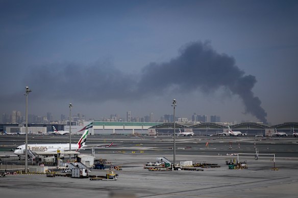 A plume of smoke caused by an Iranian strike is seen in the background as Emirates planes are parked at Dubai International Airport on Sunday.