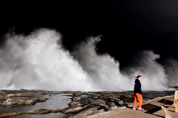 A person walks past large breaking waves at Clovelly beach on Saturday morning.