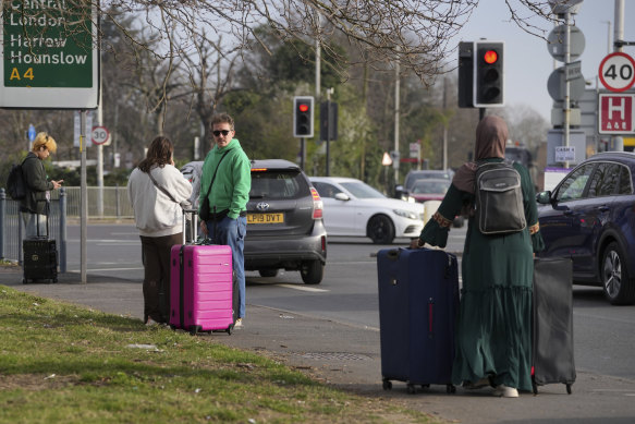 Passengers with suitcases wait on a nearby road after Heathrow Airport closed.
