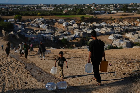 Displaced Palestinians carry water containers near a tent camp in Deir al-Balah, central Gaza Strip.