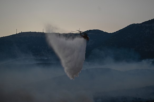 A firefighting helicopter drops water over a smoke-filled forest during a wildfire near Porto Germeno.