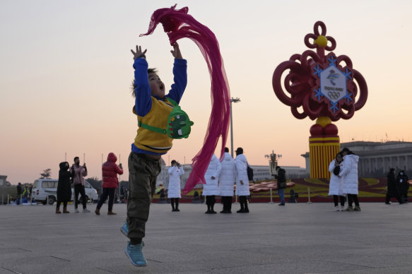 A child plays with a red scarf near a decoration for the Beijing Winter Olympics on Tiananmen Square in Beijing, China.