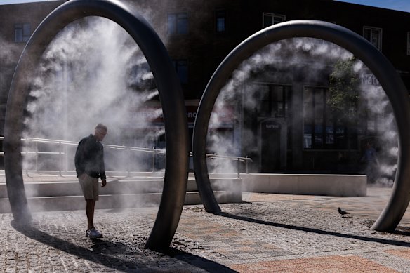 Members of the public walk through a piece of public art that sprays mist in Dover, England.