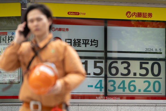 A worker walks past monitors displaying the Nikkei 225 Stock Average figure outside a securities firm in Tokyo on Monday.