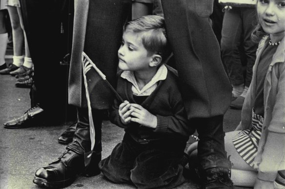 A small boy watches the march protected by a serving member of the Army.